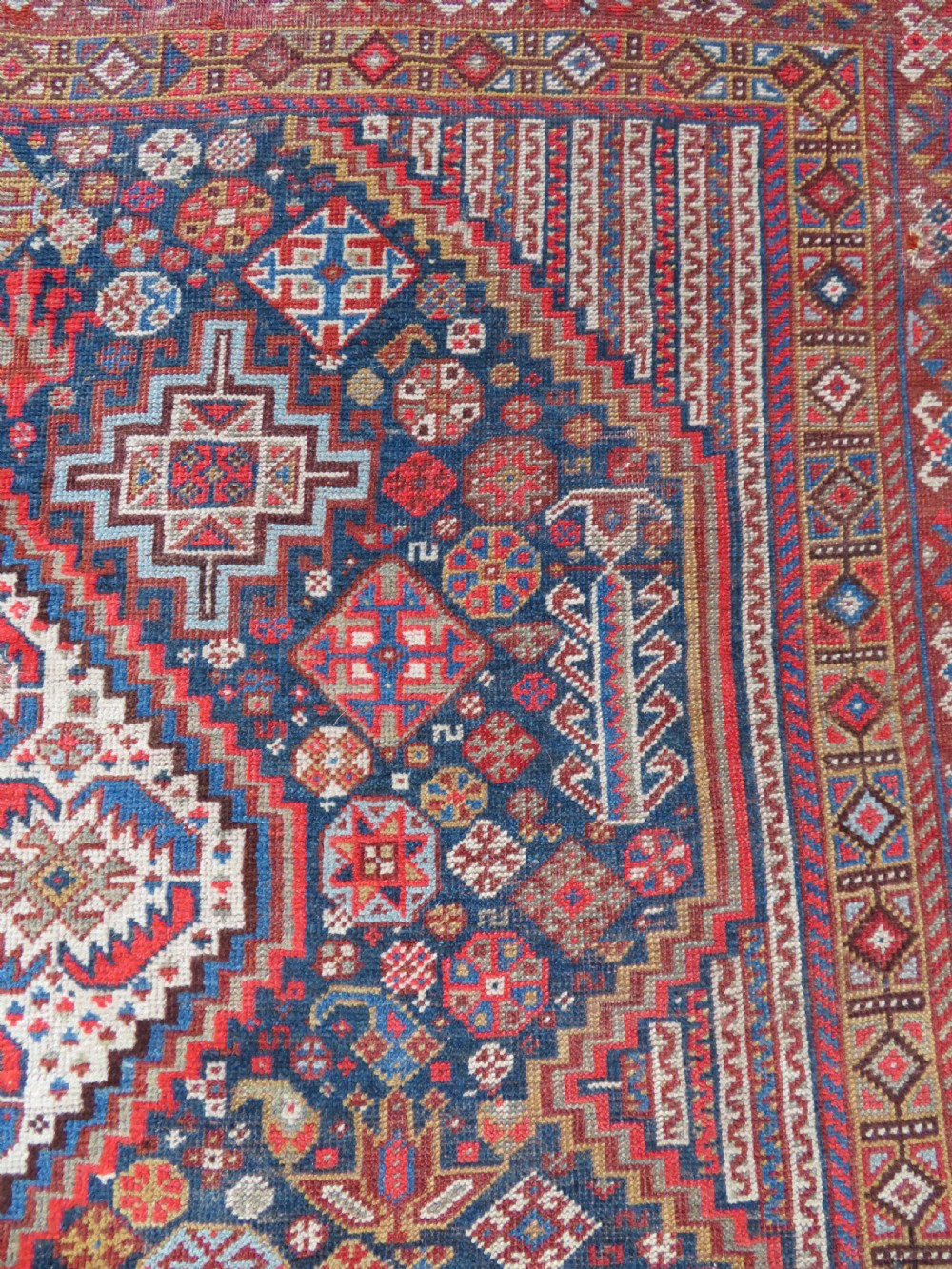An antique hand-knotted Khamseh tribal carpet featuring multiple diamond medallions and geometric borders in navy blue, terracotta red, and cream wool. View VII
