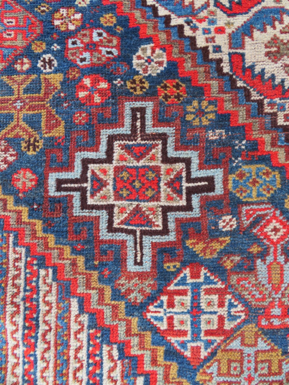 An antique hand-knotted Khamseh tribal carpet featuring multiple diamond medallions and geometric borders in navy blue, terracotta red, and cream wool. View XII