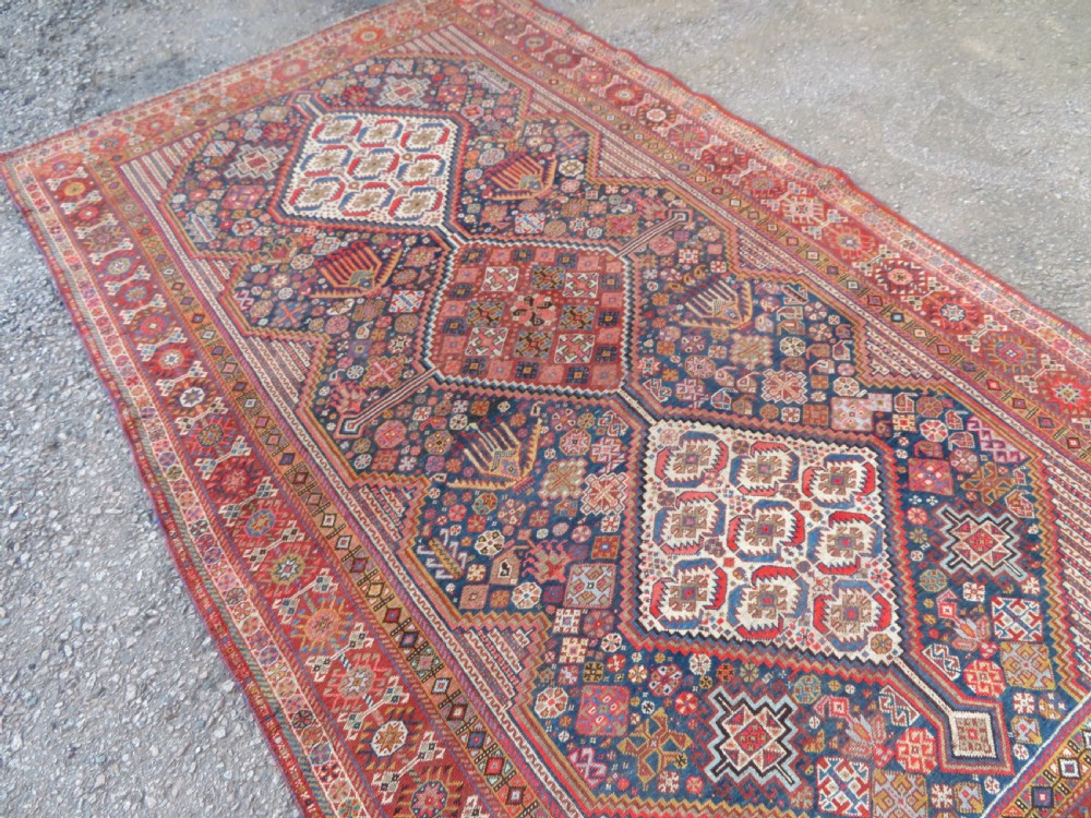 An antique hand-knotted Khamseh tribal carpet featuring multiple diamond medallions and geometric borders in navy blue, terracotta red, and cream wool. View XVII