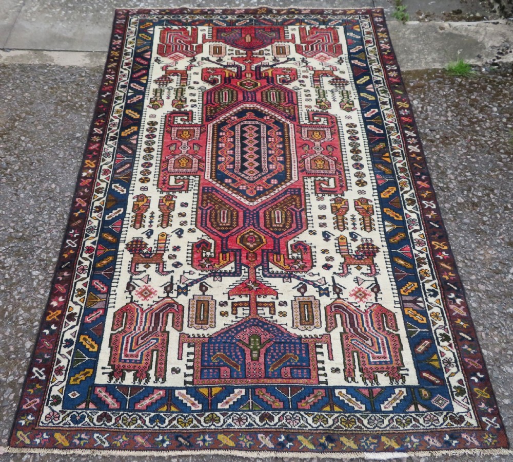 An antique hand-knotted Persian tribal rug featuring a geometric medallion and stylised animal figures in terracotta red, navy blue, and cream.