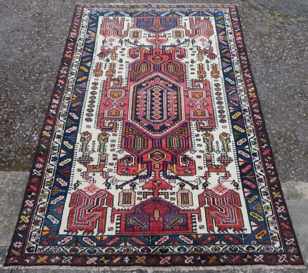 An antique hand-knotted Persian tribal rug featuring a geometric medallion and stylised animal figures in terracotta red, navy blue, and cream. View II