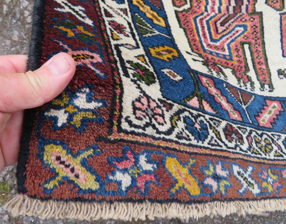 An antique hand-knotted Persian tribal rug featuring a geometric medallion and stylised animal figures in terracotta red, navy blue, and cream. View IV