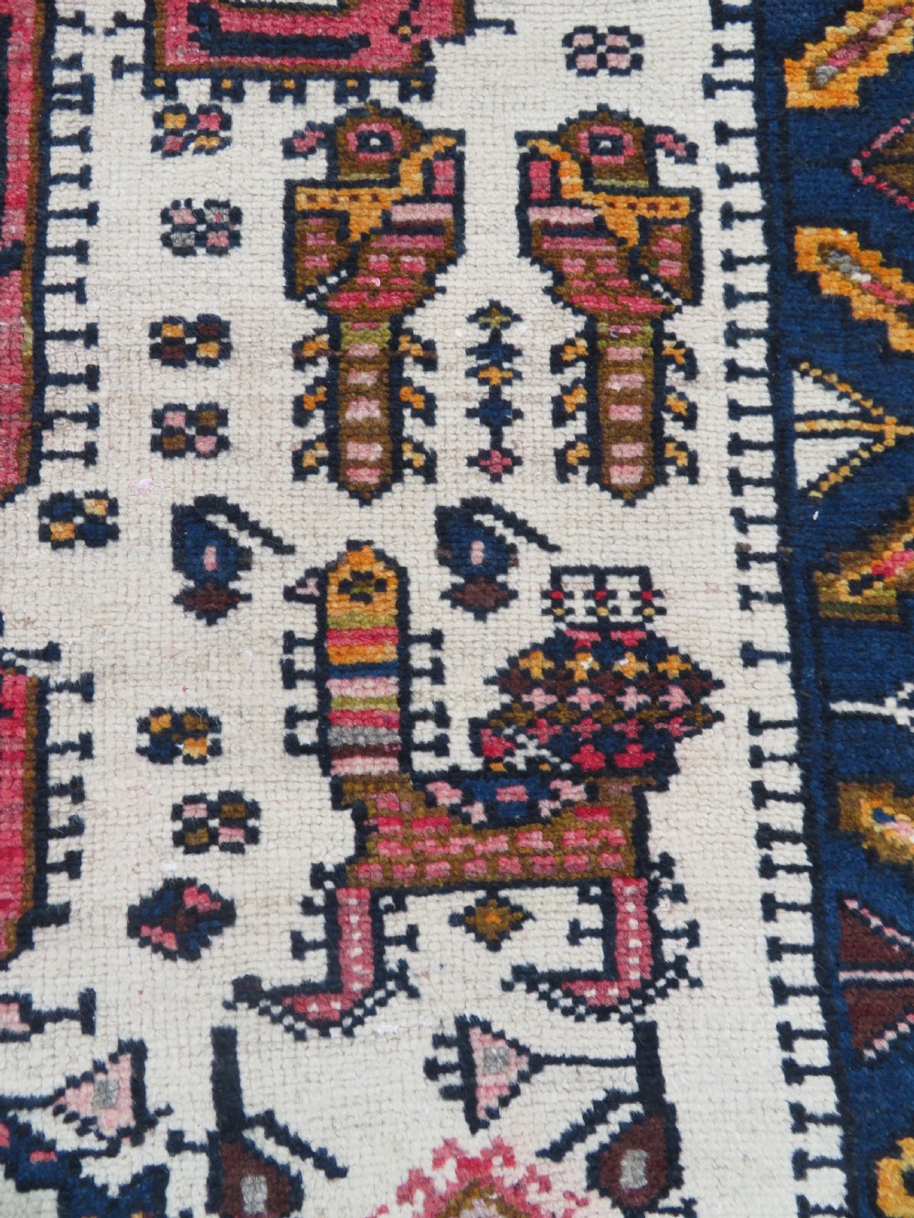 An antique hand-knotted Persian tribal rug featuring a geometric medallion and stylised animal figures in terracotta red, navy blue, and cream. View VI