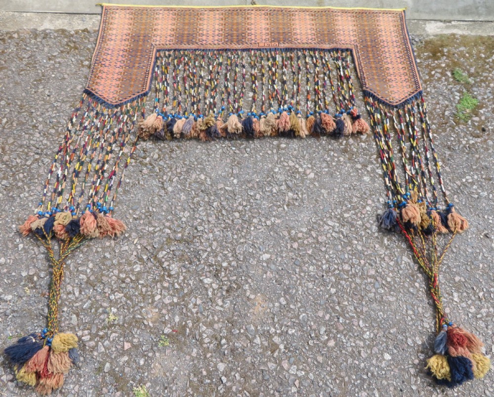 A handwoven arch-shaped Ersari kapunuk textile with geometric terracotta motifs and long decorative wool tassels dangling from the base.