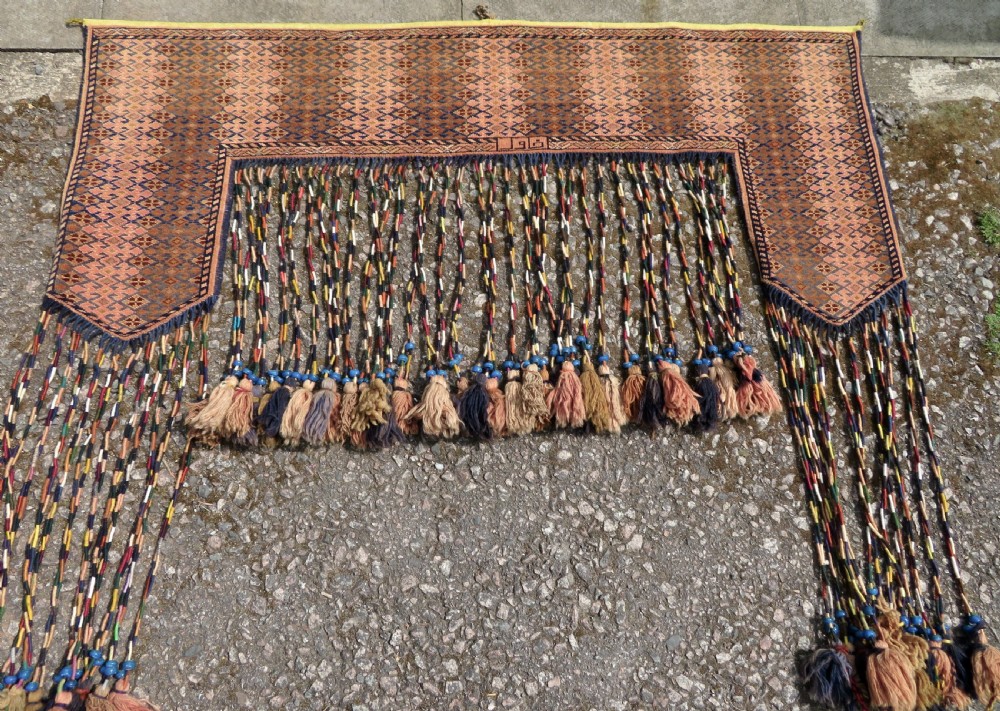 A handwoven arch-shaped Ersari kapunuk textile with geometric terracotta motifs and long decorative wool tassels dangling from the base. View III