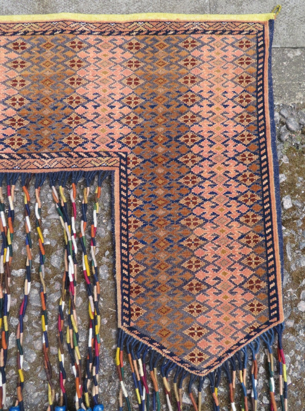 A handwoven arch-shaped Ersari kapunuk textile with geometric terracotta motifs and long decorative wool tassels dangling from the base. View V