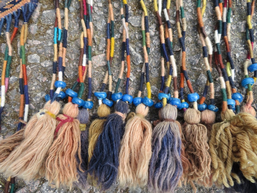 A handwoven arch-shaped Ersari kapunuk textile with geometric terracotta motifs and long decorative wool tassels dangling from the base. View VI