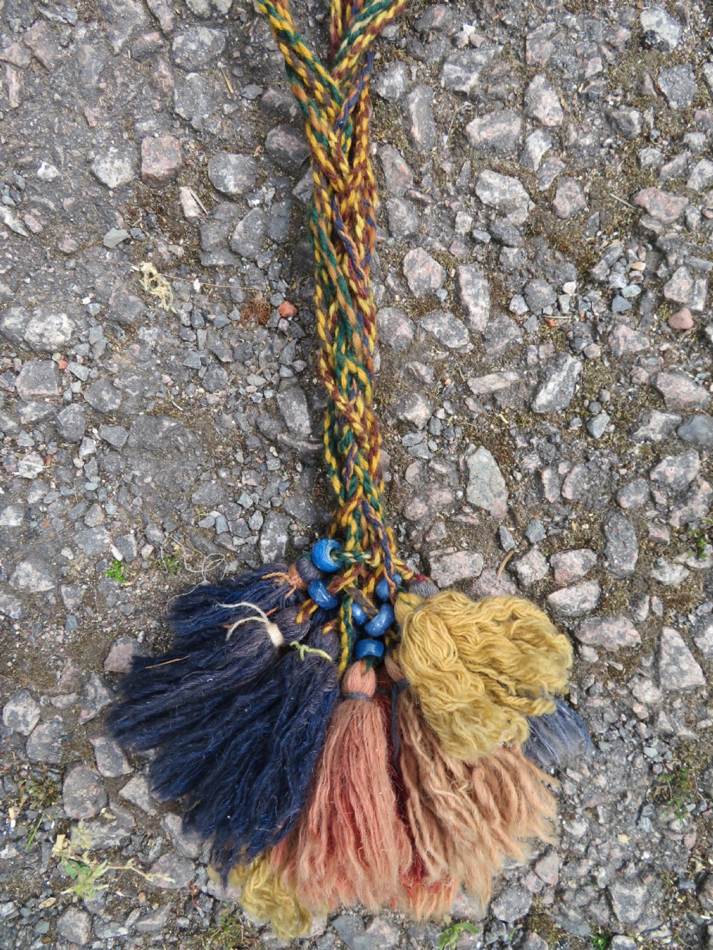 A handwoven arch-shaped Ersari kapunuk textile with geometric terracotta motifs and long decorative wool tassels dangling from the base. View X
