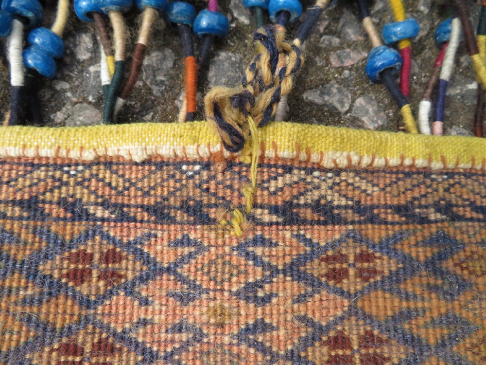 A handwoven arch-shaped Ersari kapunuk textile with geometric terracotta motifs and long decorative wool tassels dangling from the base. View XII