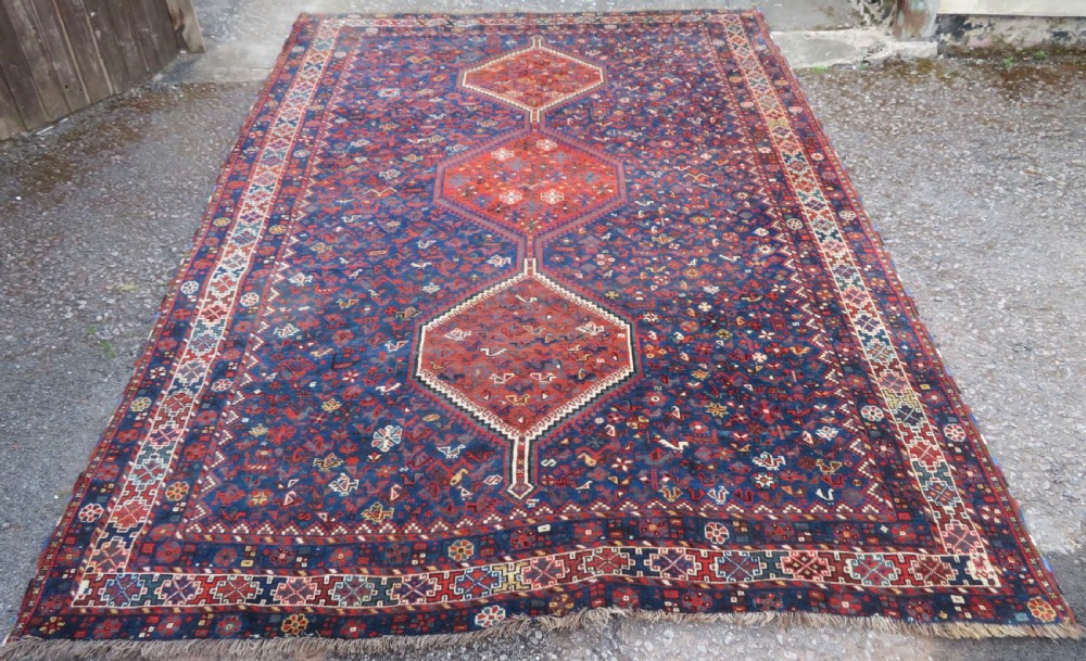 An antique Persian Khamseh carpet featuring three diamond-shaped central medallions and small bird motifs on a dark navy blue field with geometric borders.