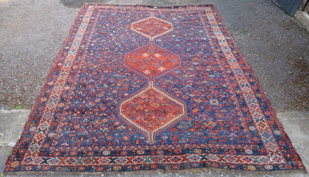 An antique Persian Khamseh carpet featuring three diamond-shaped central medallions and small bird motifs on a dark navy blue field with geometric borders. View II