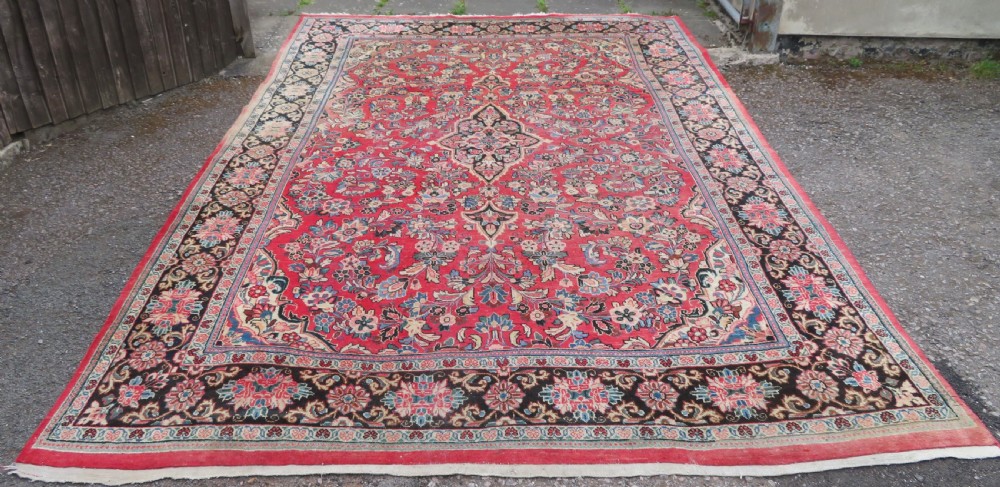 A large hand-knotted Sarouk Persian carpet featuring a dense red floral ground, central medallion, and elaborate dark borders.