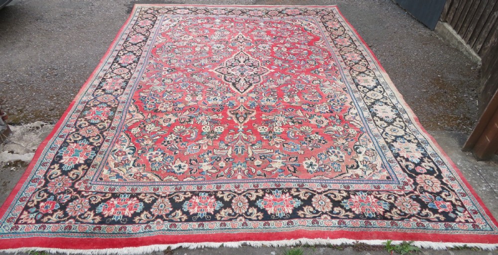 A large hand-knotted Sarouk Persian carpet featuring a dense red floral ground, central medallion, and elaborate dark borders. View II