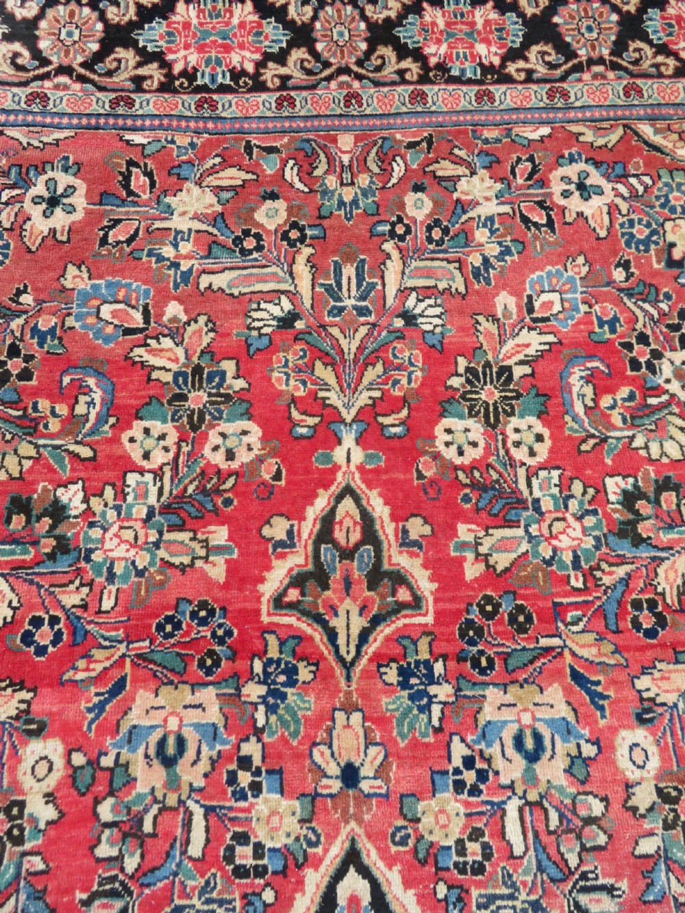 A large hand-knotted Sarouk Persian carpet featuring a dense red floral ground, central medallion, and elaborate dark borders. View V