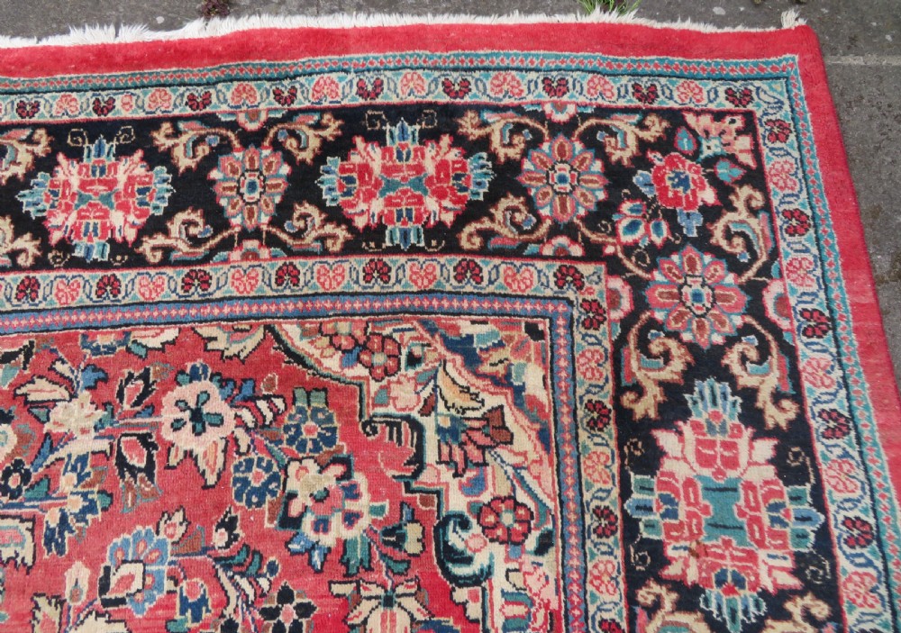 A large hand-knotted Sarouk Persian carpet featuring a dense red floral ground, central medallion, and elaborate dark borders. View VI