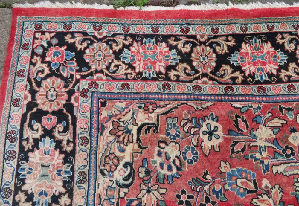 A large hand-knotted Sarouk Persian carpet featuring a dense red floral ground, central medallion, and elaborate dark borders. View VII