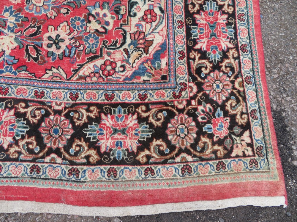 A large hand-knotted Sarouk Persian carpet featuring a dense red floral ground, central medallion, and elaborate dark borders. View IX