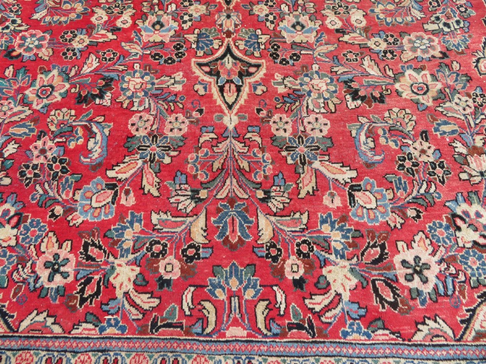 A large hand-knotted Sarouk Persian carpet featuring a dense red floral ground, central medallion, and elaborate dark borders. View X