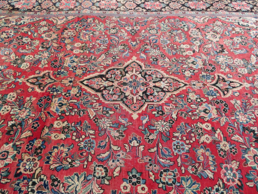 A large hand-knotted Sarouk Persian carpet featuring a dense red floral ground, central medallion, and elaborate dark borders. View XII
