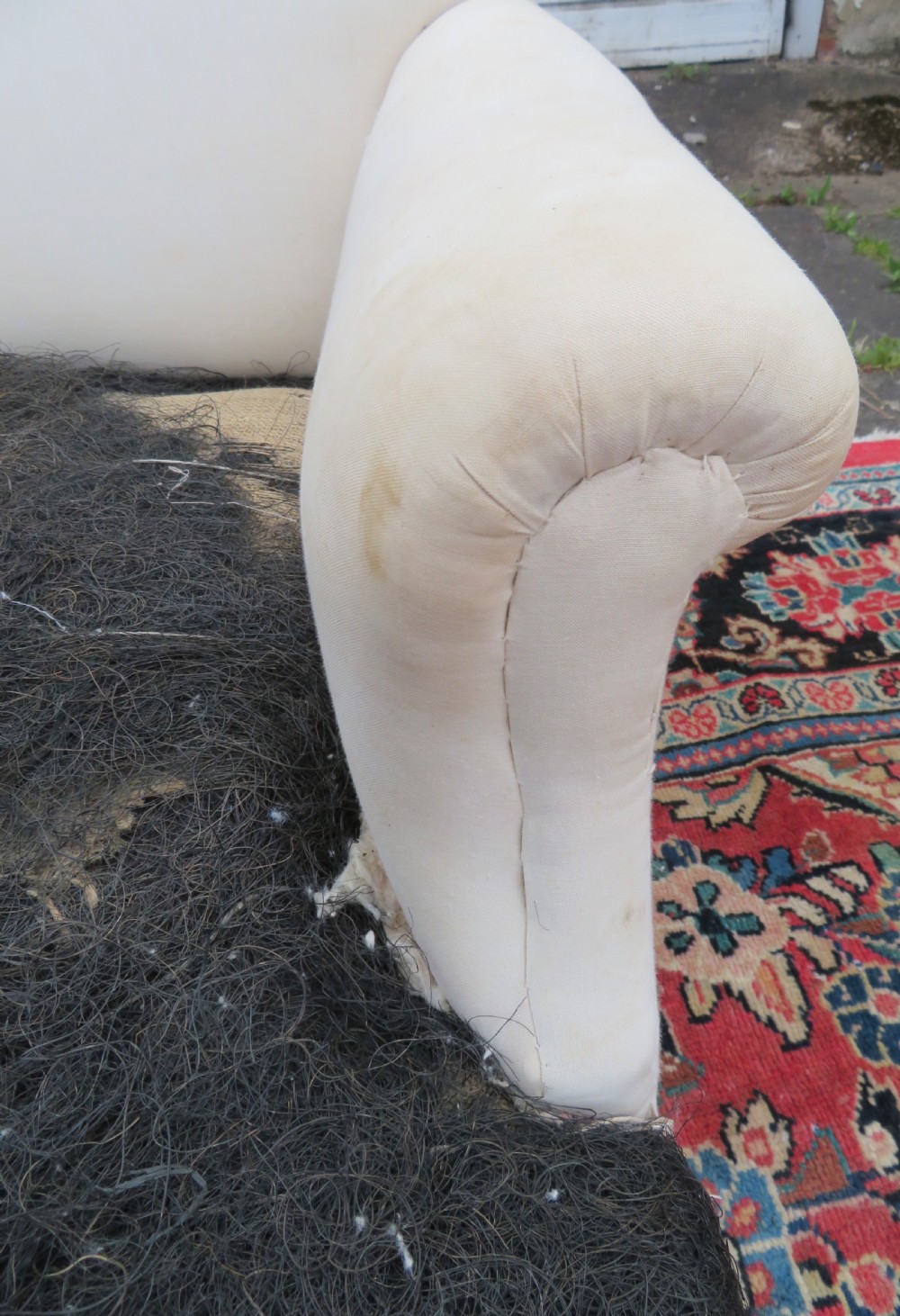 A Howard style low easy chair frame with exposed horsehair seat filling, cream calico back, and turned front wooden legs on ceramic castors. View V