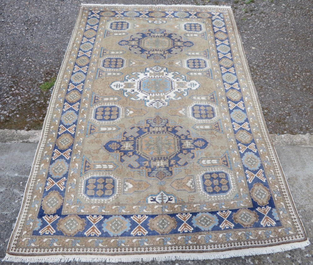 A hand-knotted North Persian Ardabil wool rug featuring three central geometric medallions in blue, cream, and beige on a neutral field with patterned borders.