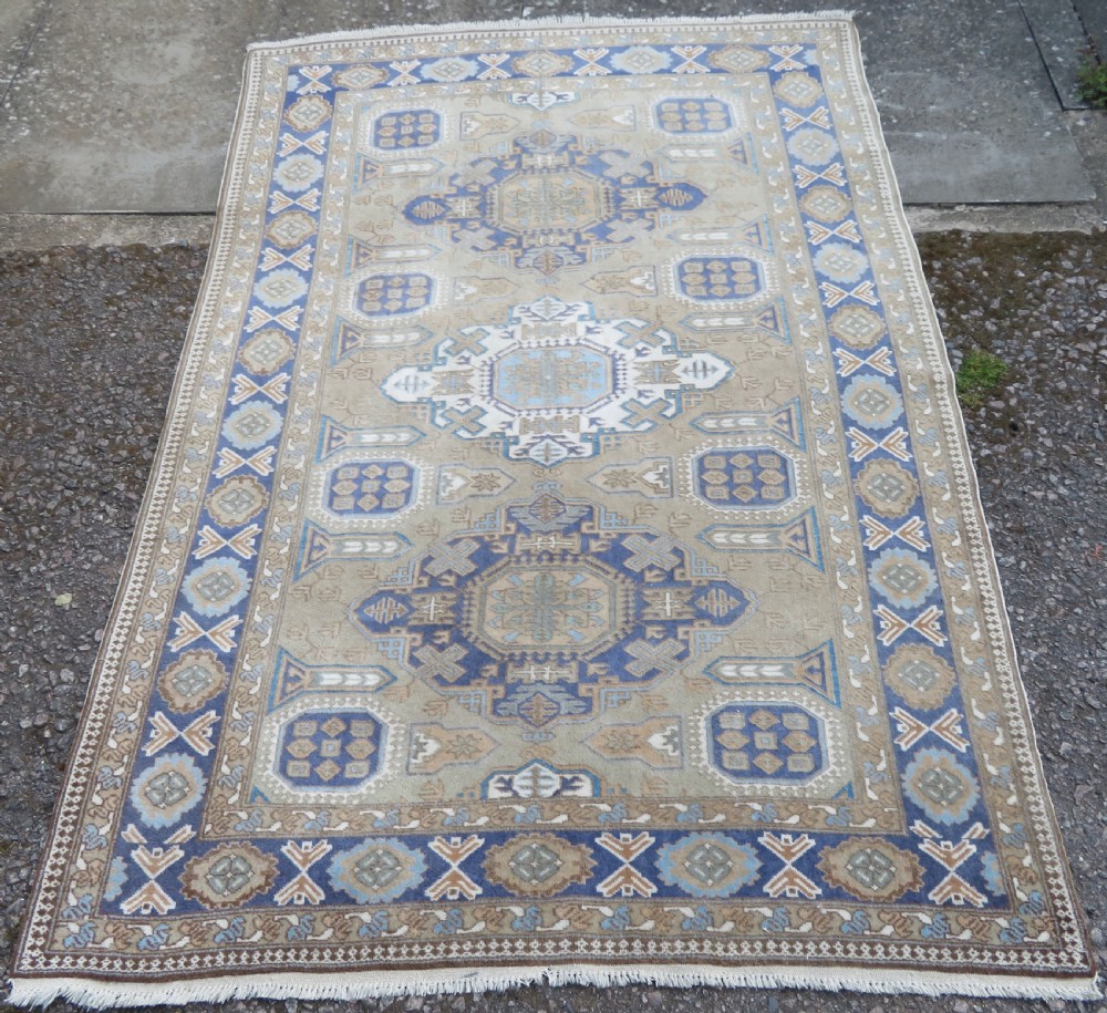 A hand-knotted North Persian Ardabil wool rug featuring three central geometric medallions in blue, cream, and beige on a neutral field with patterned borders. View II