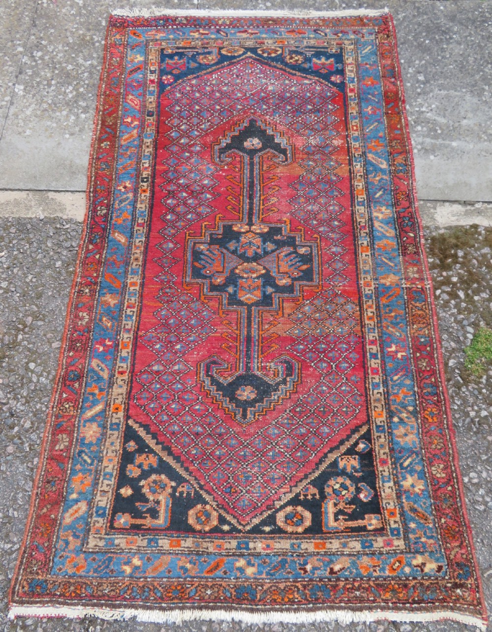 An antique hand-knotted Persian Sarab rug featuring a central dark blue geometric medallion on a red patterned field with light blue borders.