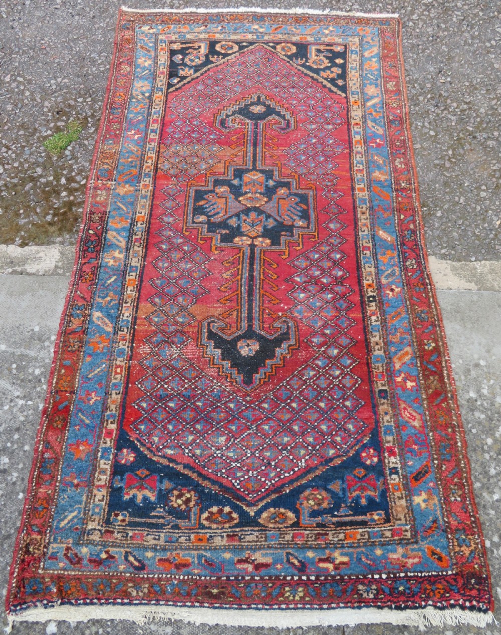 An antique hand-knotted Persian Sarab rug featuring a central dark blue geometric medallion on a red patterned field with light blue borders. View II