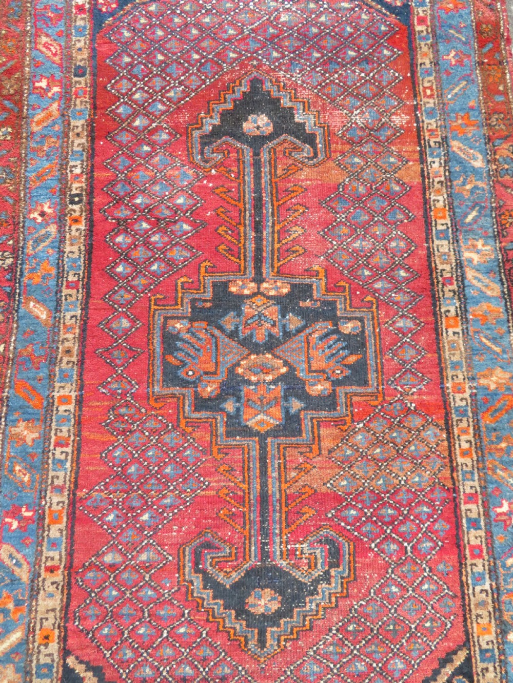 An antique hand-knotted Persian Sarab rug featuring a central dark blue geometric medallion on a red patterned field with light blue borders. View III