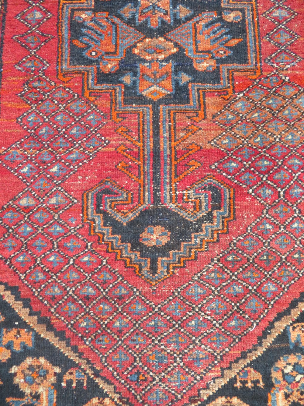 An antique hand-knotted Persian Sarab rug featuring a central dark blue geometric medallion on a red patterned field with light blue borders. View IX