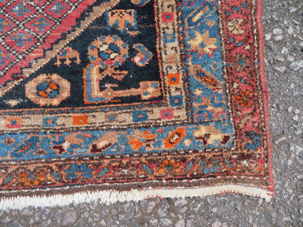 An antique hand-knotted Persian Sarab rug featuring a central dark blue geometric medallion on a red patterned field with light blue borders. View XI