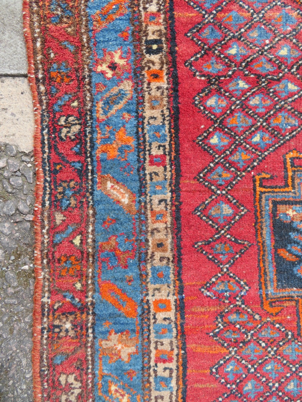 An antique hand-knotted Persian Sarab rug featuring a central dark blue geometric medallion on a red patterned field with light blue borders. View XII