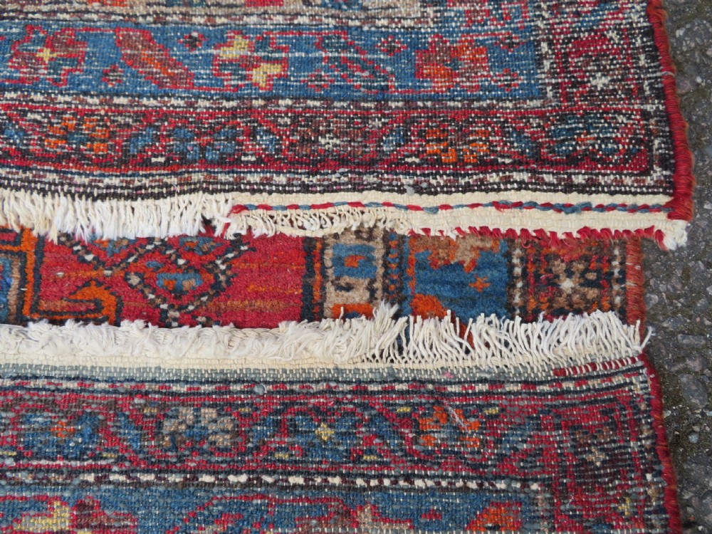 An antique hand-knotted Persian Sarab rug featuring a central dark blue geometric medallion on a red patterned field with light blue borders. View XIV