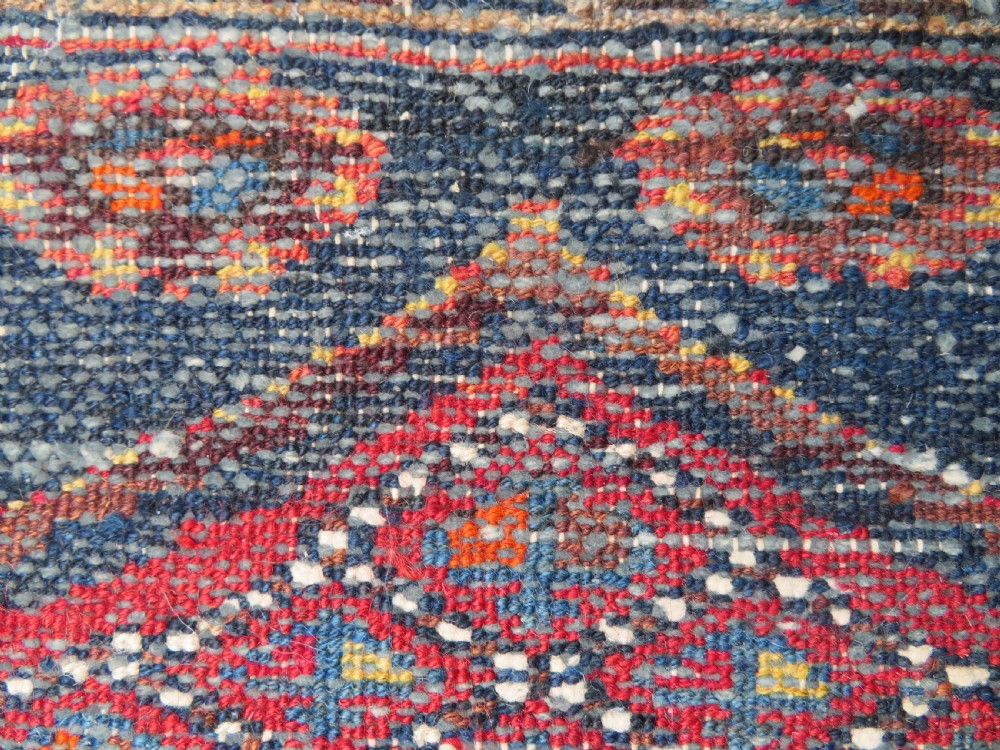 An antique hand-knotted Persian Sarab rug featuring a central dark blue geometric medallion on a red patterned field with light blue borders. View XV