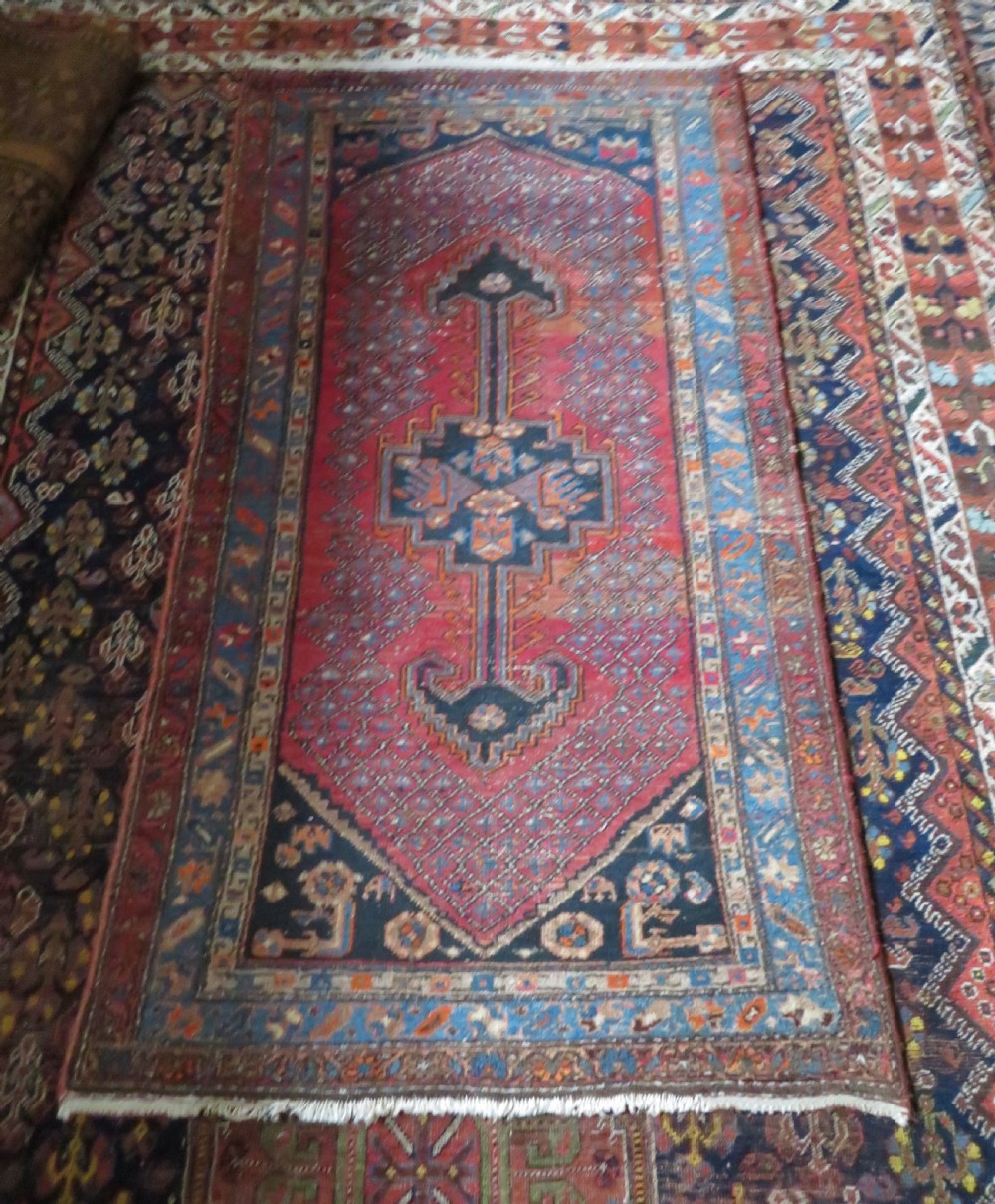 An antique hand-knotted Persian Sarab rug featuring a central dark blue geometric medallion on a red patterned field with light blue borders. View XVI
