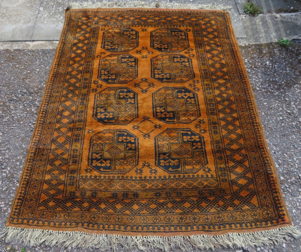 A rectangular hand-knotted Afghan wool rug with dark blue octagonal gul motifs set against a rich gold field with geometric borders.