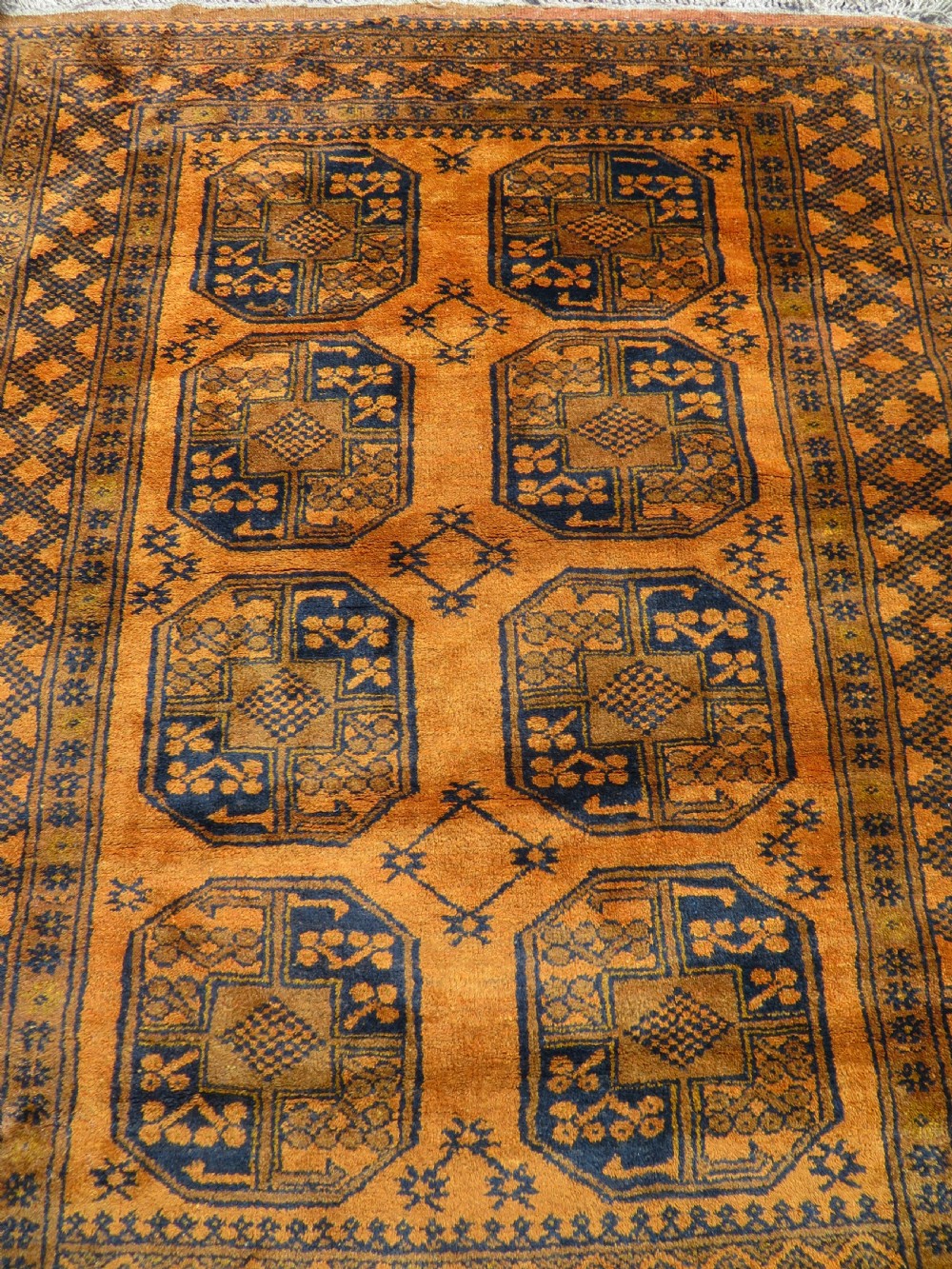 A rectangular hand-knotted Afghan wool rug with dark blue octagonal gul motifs set against a rich gold field with geometric borders. View II