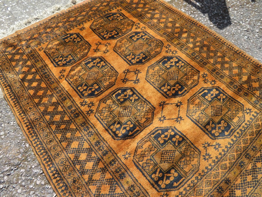 A rectangular hand-knotted Afghan wool rug with dark blue octagonal gul motifs set against a rich gold field with geometric borders. View IV