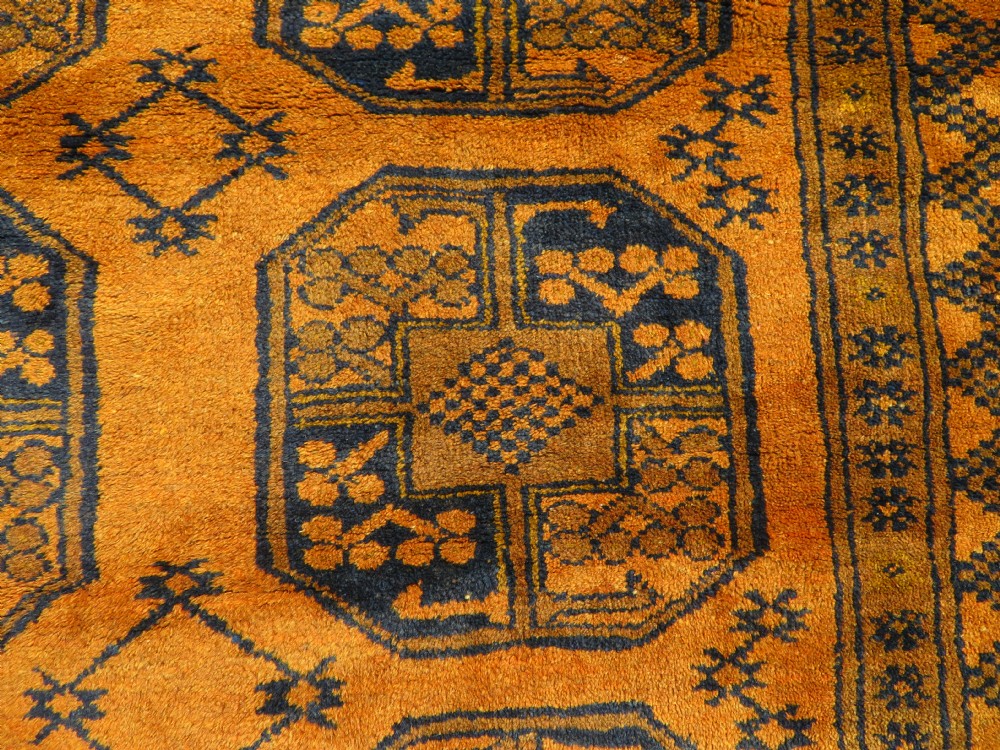 A rectangular hand-knotted Afghan wool rug with dark blue octagonal gul motifs set against a rich gold field with geometric borders. View VI