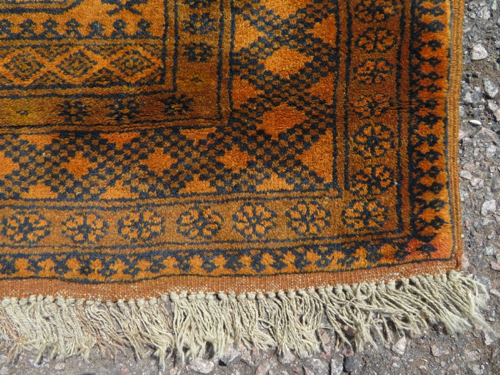 A rectangular hand-knotted Afghan wool rug with dark blue octagonal gul motifs set against a rich gold field with geometric borders. View IX