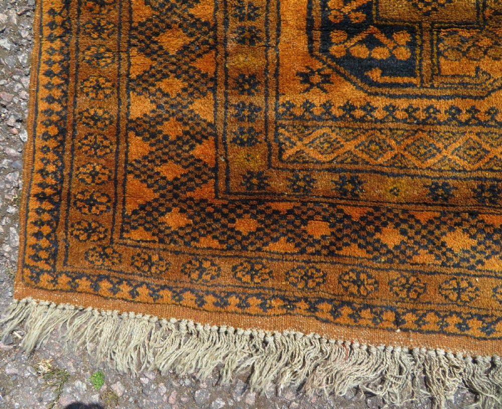 A rectangular hand-knotted Afghan wool rug with dark blue octagonal gul motifs set against a rich gold field with geometric borders. View X