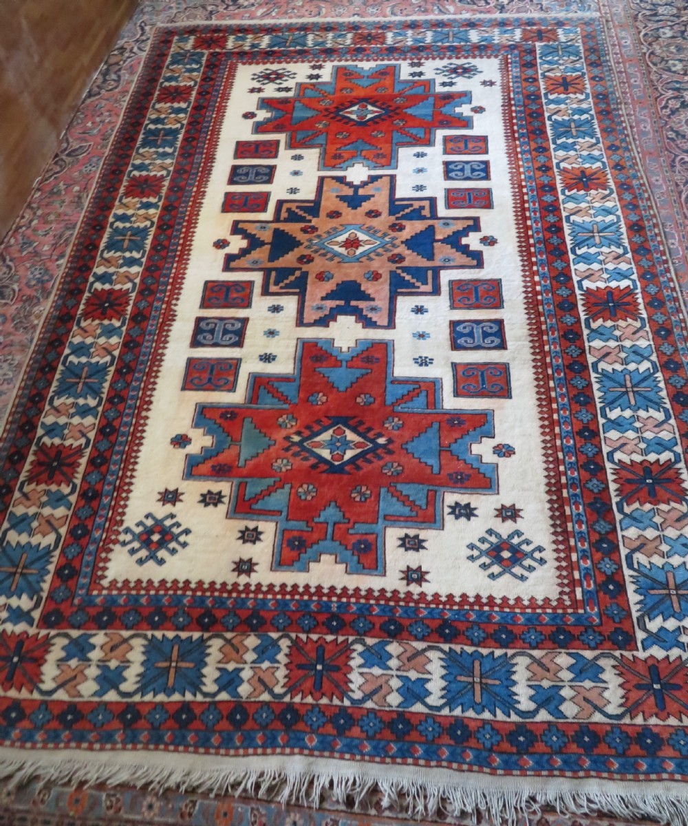 A hand-knotted wool carpet featuring three large geometric medallions in red, blue, and terracotta on a cream field, framed by multi-layered geometric borders.
