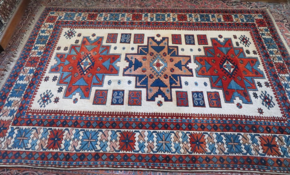 A hand-knotted wool carpet featuring three large geometric medallions in red, blue, and terracotta on a cream field, framed by multi-layered geometric borders. View II
