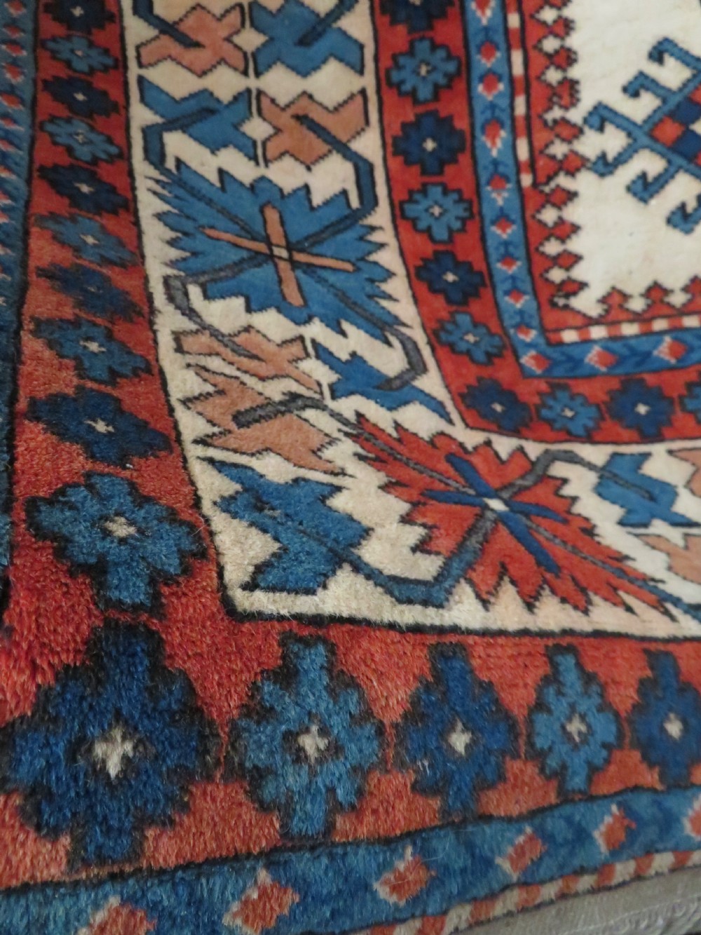 A hand-knotted wool carpet featuring three large geometric medallions in red, blue, and terracotta on a cream field, framed by multi-layered geometric borders. View VII