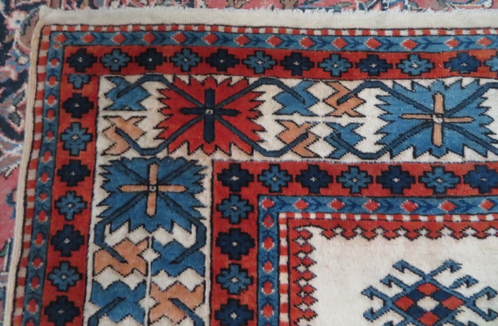 A hand-knotted wool carpet featuring three large geometric medallions in red, blue, and terracotta on a cream field, framed by multi-layered geometric borders. View IX