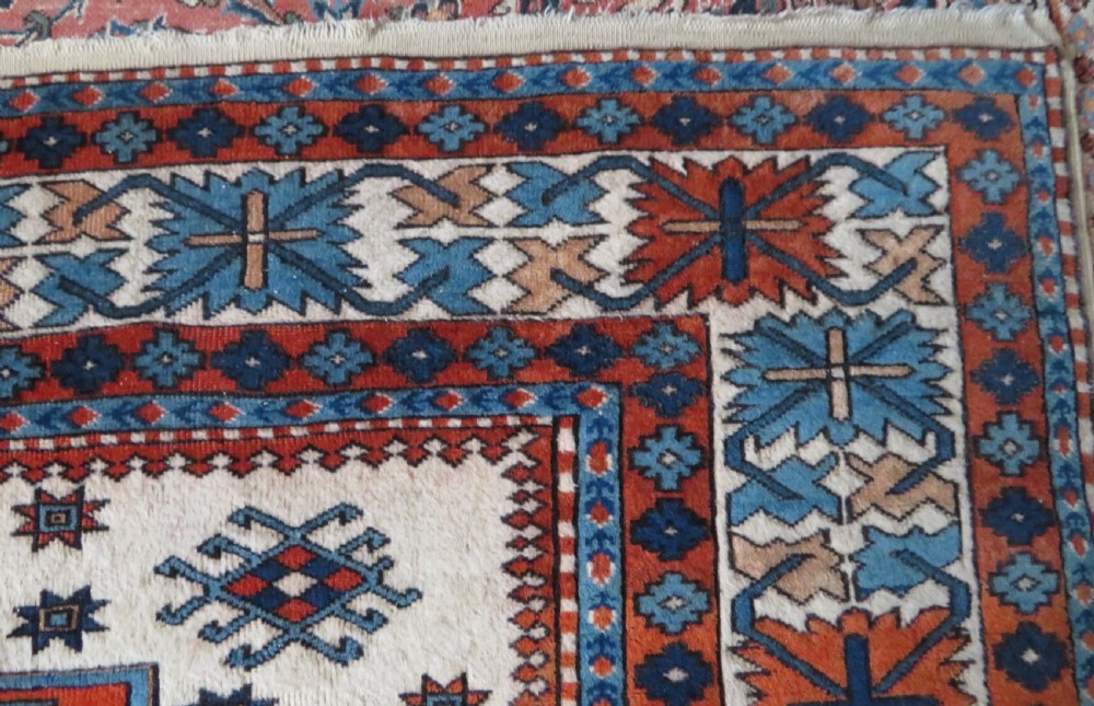 A hand-knotted wool carpet featuring three large geometric medallions in red, blue, and terracotta on a cream field, framed by multi-layered geometric borders. View X