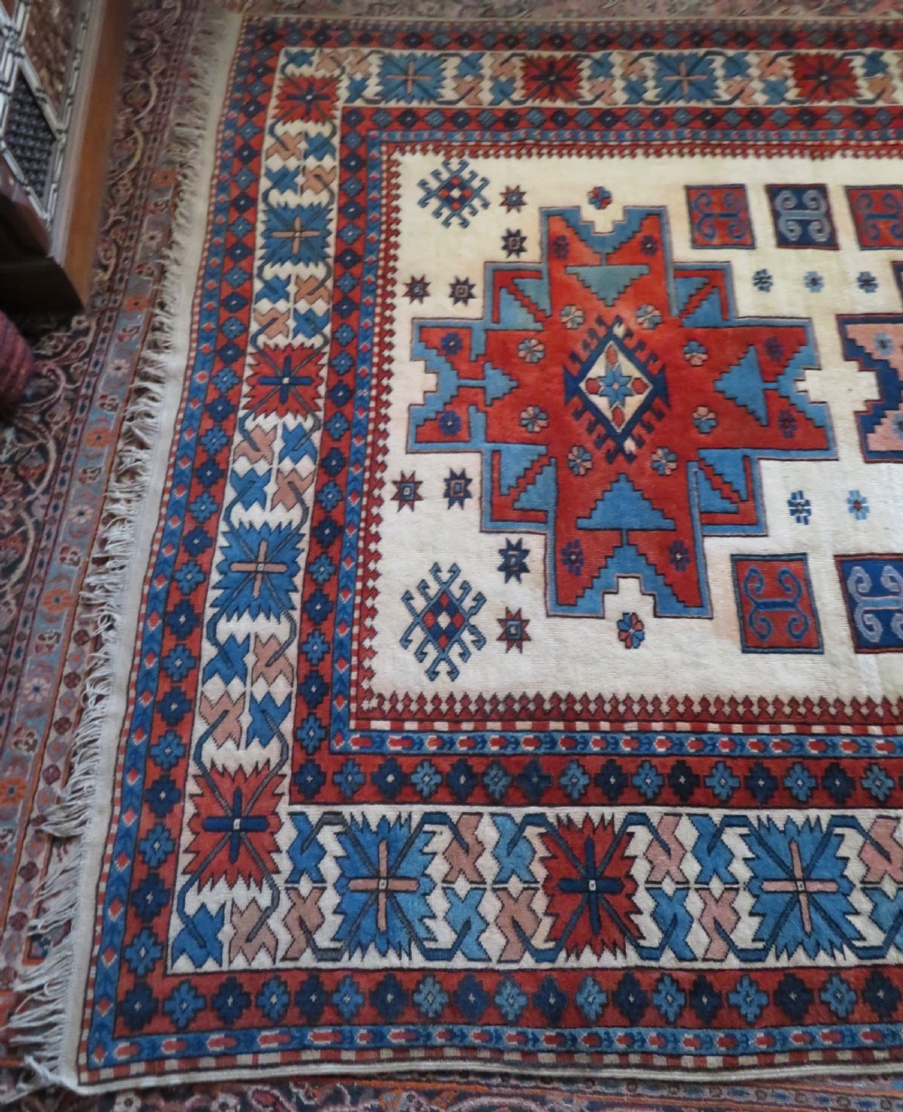 A hand-knotted wool carpet featuring three large geometric medallions in red, blue, and terracotta on a cream field, framed by multi-layered geometric borders. View XI