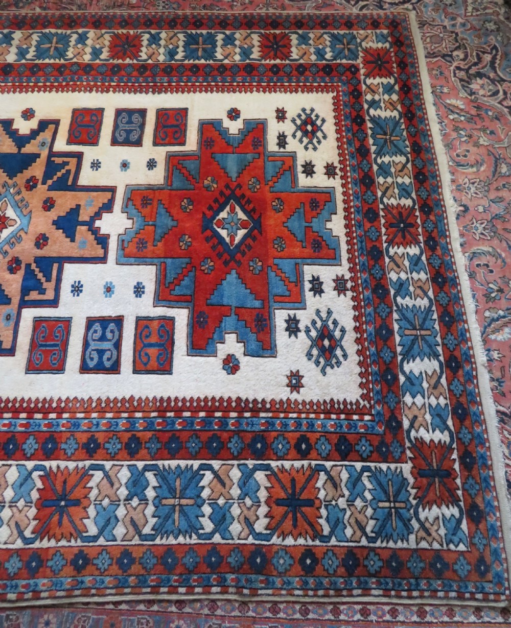 A hand-knotted wool carpet featuring three large geometric medallions in red, blue, and terracotta on a cream field, framed by multi-layered geometric borders. View XII