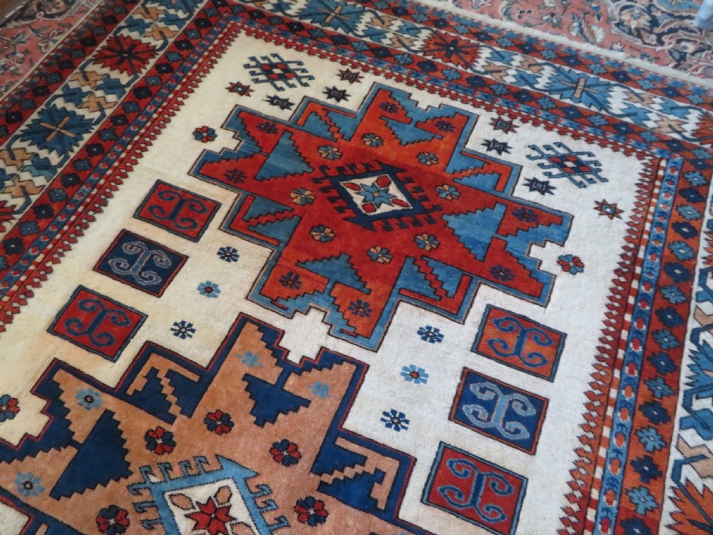 A hand-knotted wool carpet featuring three large geometric medallions in red, blue, and terracotta on a cream field, framed by multi-layered geometric borders. View XIII
