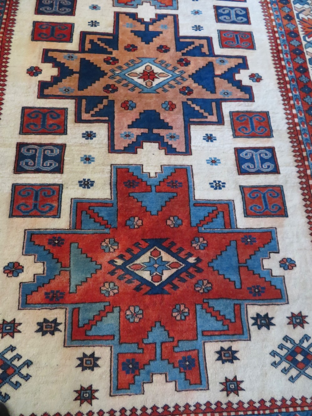 A hand-knotted wool carpet featuring three large geometric medallions in red, blue, and terracotta on a cream field, framed by multi-layered geometric borders. View XIV